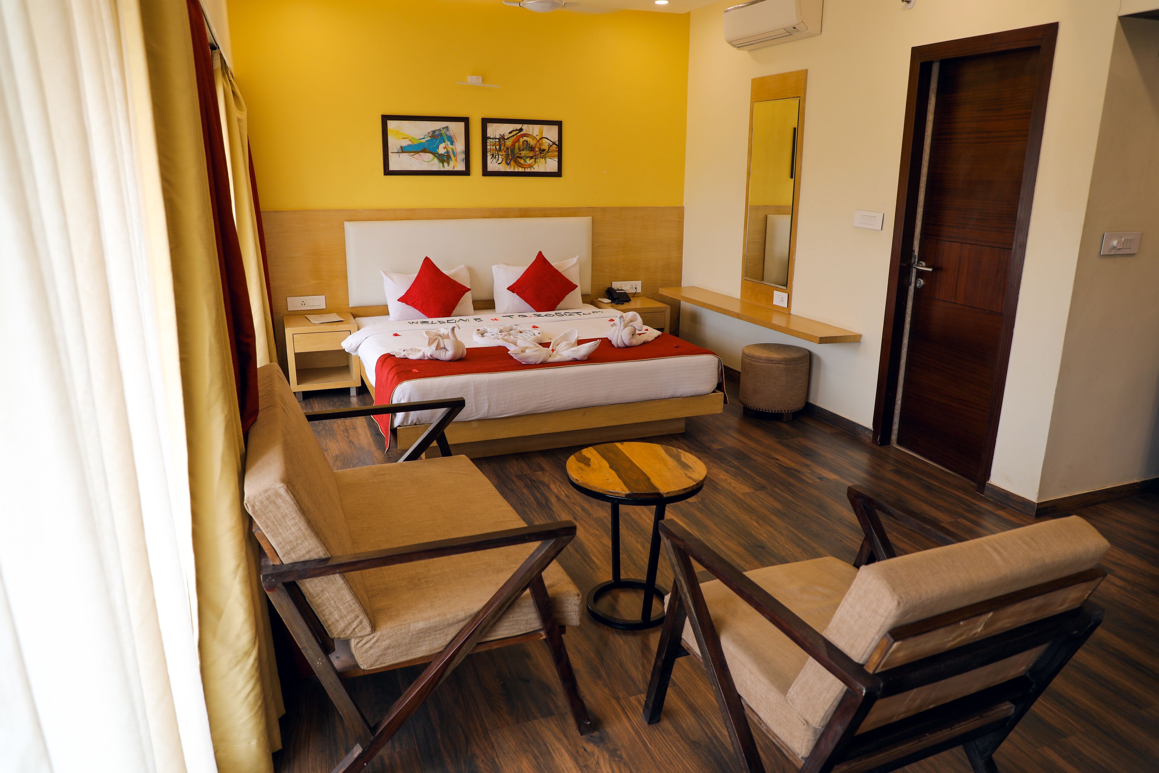 A hotel room with a bed, two nightstands, a round table, two chairs, a mirror, and artwork on the wall.