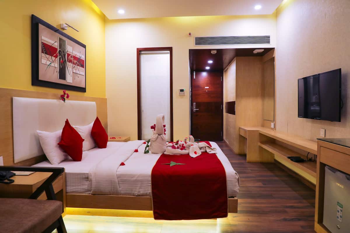 A hotel room with a bed, a TV, a desk, and a bench.