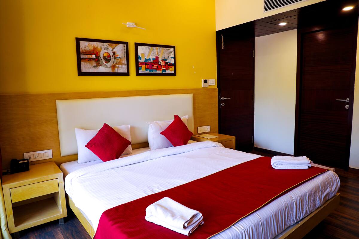 A hotel room with a large bed, red and white bedding, two paintings on the wall, and a wooden wardrobe.
