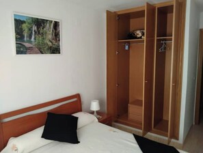 Quarto com cama, guarda-roupa de madeira, mesa de cabeceira, luminária e quadro na parede.