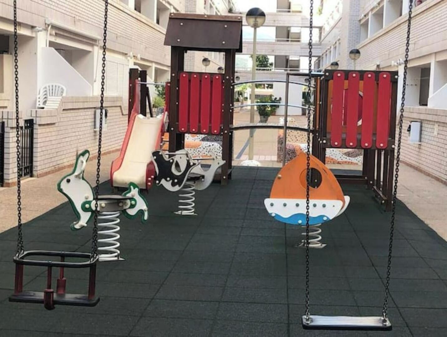 Ein Spielplatz mit Schaukeln und Rutschen, umgeben von Gebäuden.