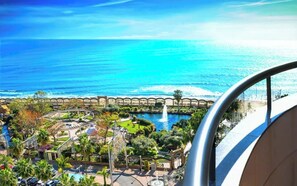 Um resort com piscina, palmeiras e vista para o oceano.