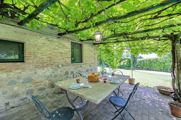 A stone-walled outdoor patio with a table set for dining, surrounded by chairs and potted plants.