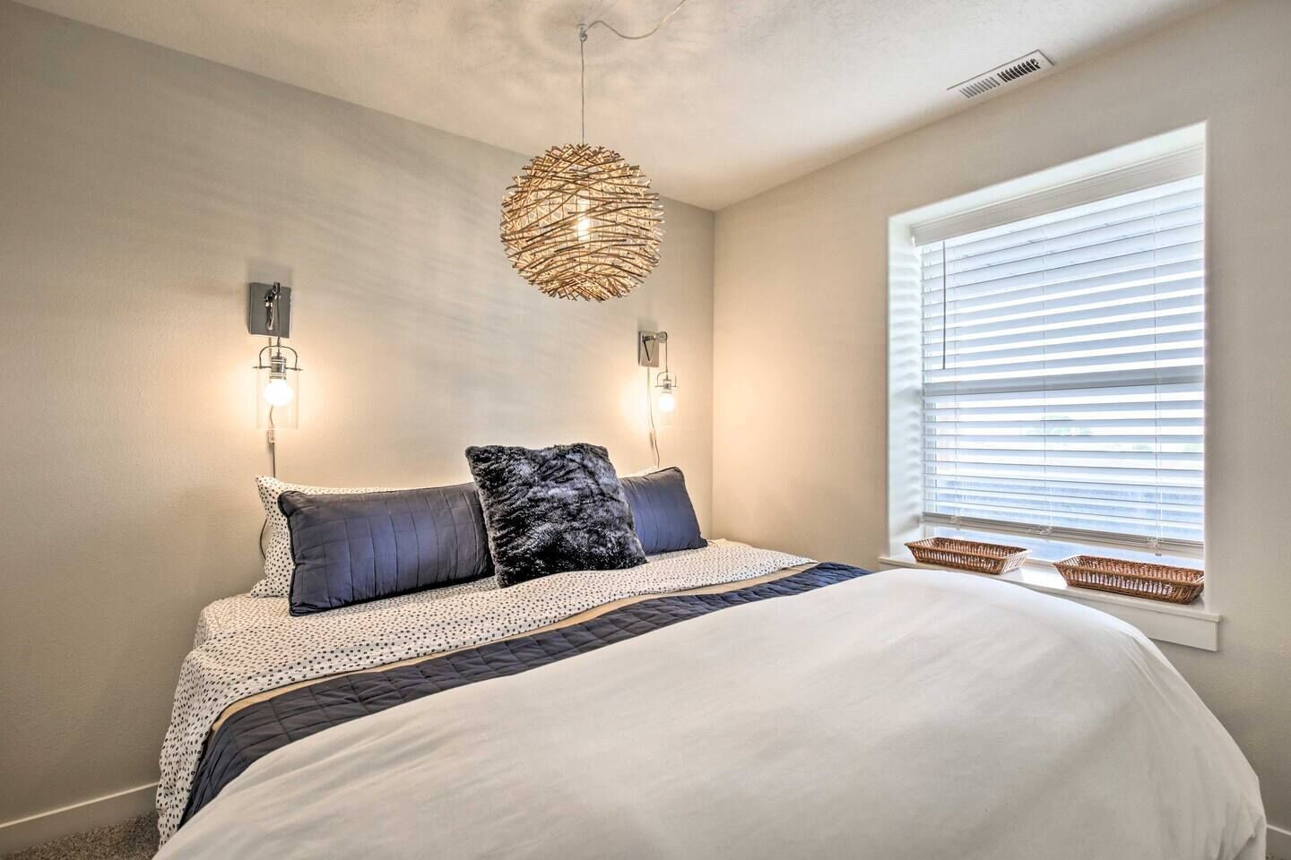 Un dormitorio con una cama grande, dos lámparas de pared, una lámpara colgante y una ventana con persianas.