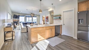 A modern kitchen with wooden cabinets, a central island, and stainless steel appliances. - Ocean Views + Hot Tub | Walk Harbor | Crab Cooker | Sleeps 6 (Depoe Bay)