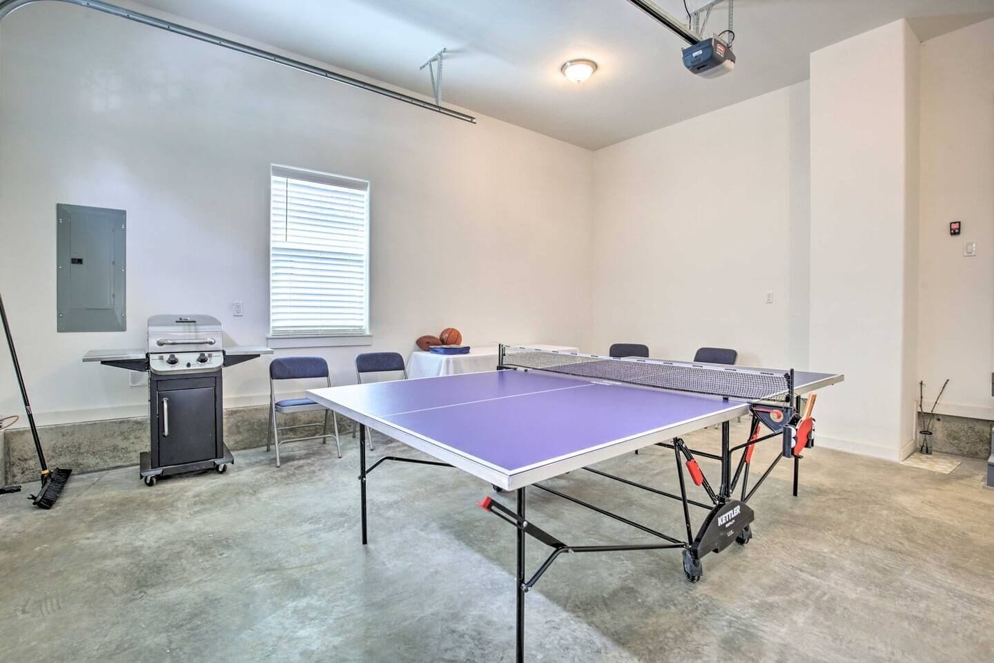 Une pièce équipée d’une table de ping-pong, d’un barbecue, de chaises et d’une fenêtre avec des stores.