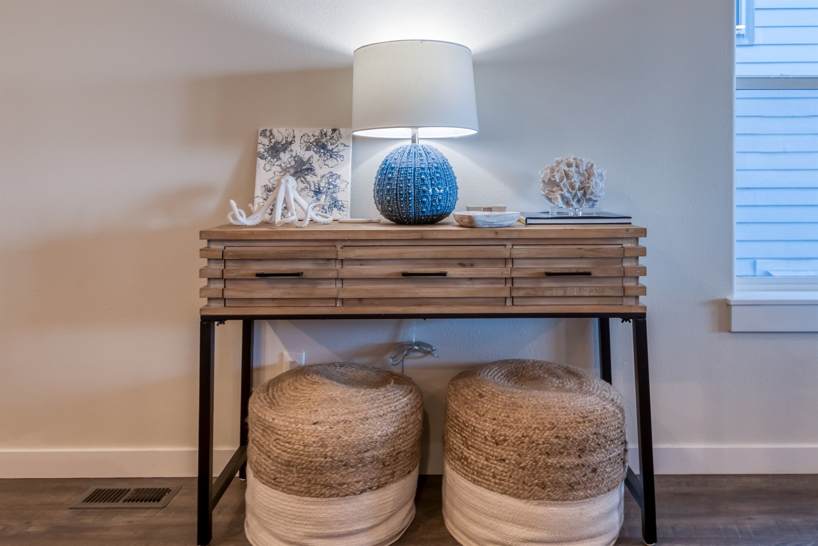 A wooden console table with a blue lamp, two woven poufs, and decorative items.