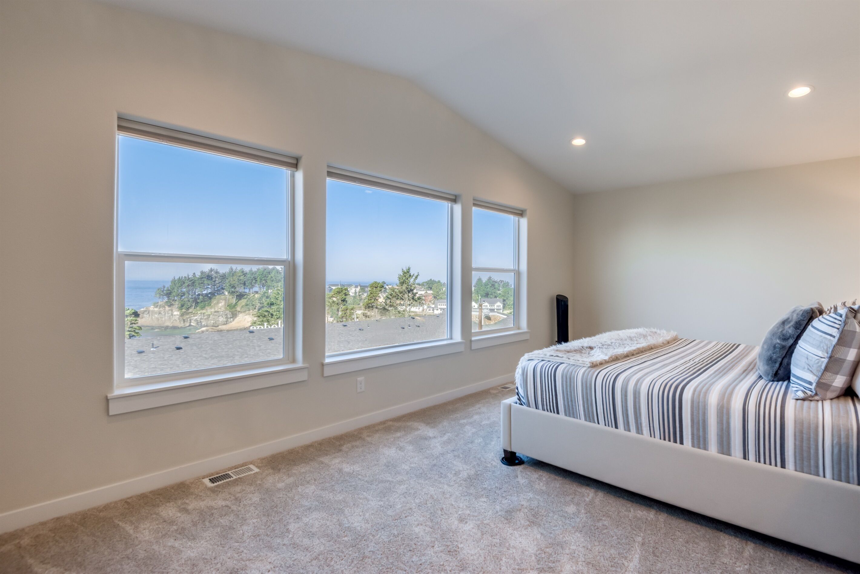 Un dormitorio con una cama grande, tres ventanas y vista al mar.