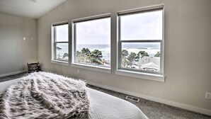 A bedroom with three large windows offering a view of the ocean and a beach. - Ocean Views + Hot Tub | Walk Harbor | Crab Cooker | Sleeps 6 (Depoe Bay)