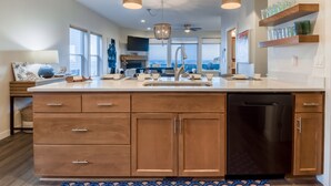 A modern kitchen with a large island, wooden cabinets, and a dishwasher. - Ocean Views + Hot Tub | Walk Harbor | Crab Cooker | Sleeps 6 (Depoe Bay)