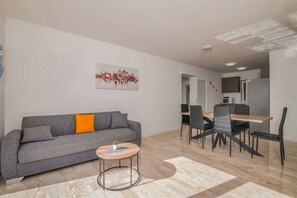 A modern living room with a grey sofa, a small round table, and a dining area with a wooden table and chairs. - Holiday apartment with 3 bedrooms (Bogovići)
