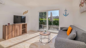 A living room with a TV, wooden cabinet, grey sofa, and a sliding glass door leading to an outdoor area.