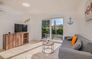 A living room with a TV, wooden cabinet, grey sofa, and a sliding glass door leading to an outdoor area. - Holiday apartment with 3 bedrooms (Bogovići)