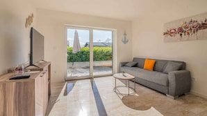 A modern living room with a sofa, a TV, a small table, and a sliding glass door leading to a balcony.