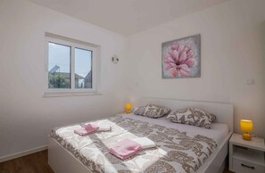 Une chambre à coucher avec un lit, deux lampes de chevet, une fenêtre et un tableau représentant des motifs floraux accroché au mur.