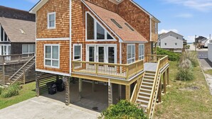 A two-story house with a wooden exterior, a balcony, and a staircase leading to the second floor. - Totally Beach'n 4 Bedroom Home in Kill Devil Hills (Kill Devil Hills)