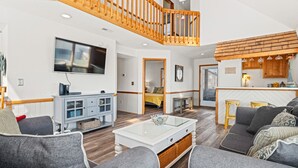 A spacious living room with a high ceiling, a wooden staircase, a kitchen area, and a dining space. - Totally Beach'n 4 Bedroom Home in Kill Devil Hills (Kill Devil Hills)