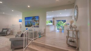 Un amplio salón con una escalera, un cuadro y vistas al exterior.