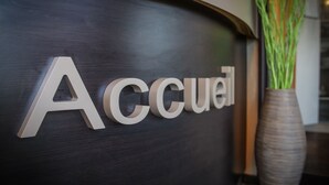 Un comptoir d’accueil avec le mot « Accueil » écrit en grandes lettres, un vase contenant des plantes vertes et une surface en bois foncé.