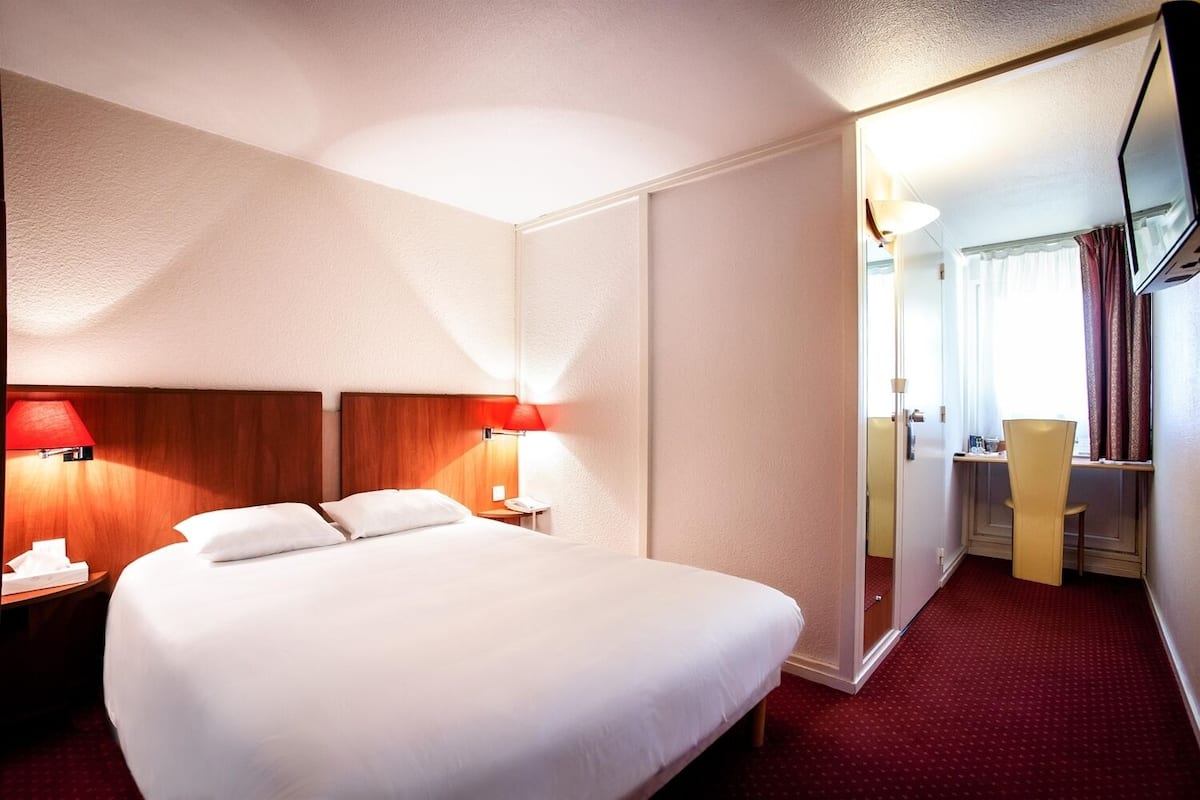 Una habitació d'hotel amb un llit gran, dues taules de nit amb làmpades, un escriptori amb una cadira i un mirall.