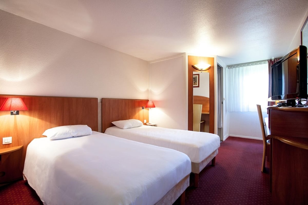 Habitació d'hotel amb dos llits, un escriptori amb televisió i un mirall.