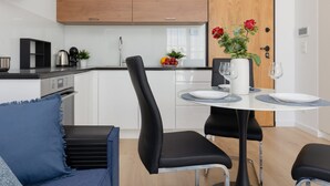 Uma cozinha moderna com armários brancos, uma porta de madeira e um espaço de refeições com uma mesa redonda posta para dois.
