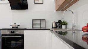 Uma cozinha moderna com forno embutido, bancada preta, pia de aço inoxidável e um vaso com planta.