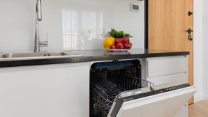 Cozinha moderna com pia de aço inoxidável, lava-louças e uma tigela de frutas no balcão.