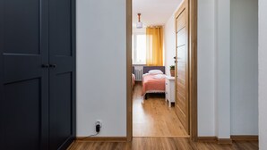 A hallway leading to a bedroom with a bed, bedside table, and a window with curtains.