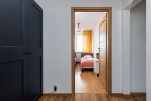 A hallway leading to a bedroom with a bed, bedside table, and a window with curtains.