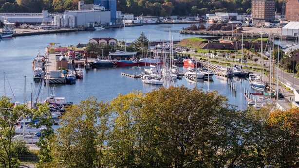A marina with boats docked, a large industrial building, and a red brick structure.