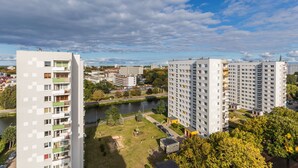 A high-rise residential building with balconies, a river, and surrounding greenery.