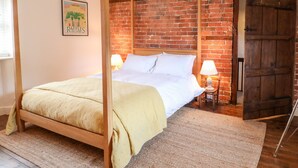 Uma cama com dossel em um quarto com paredes de tijolo aparente e porta de madeira.