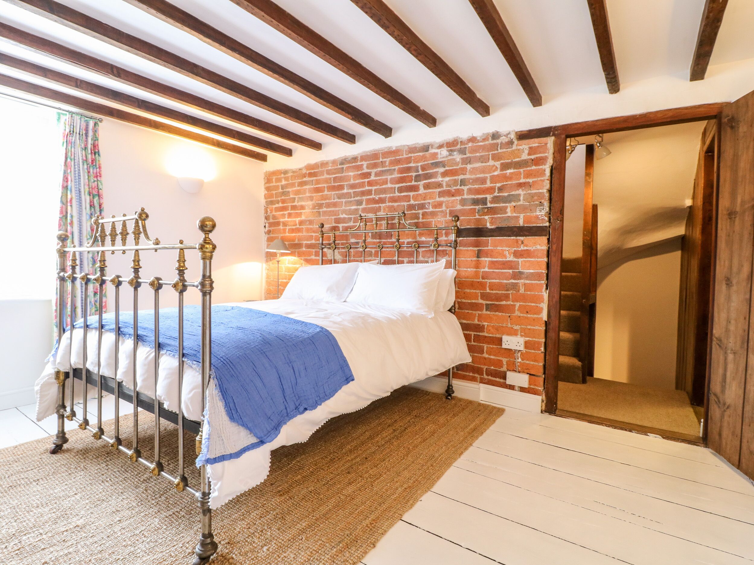 Une chambre avec un lit en métal, du linge de lit blanc, un mur en briques et un plafond en bois.