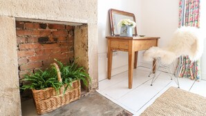 Um quarto com lareira de tijolos, uma mesa de madeira com um vaso de flores e uma poltrona aconchegante.