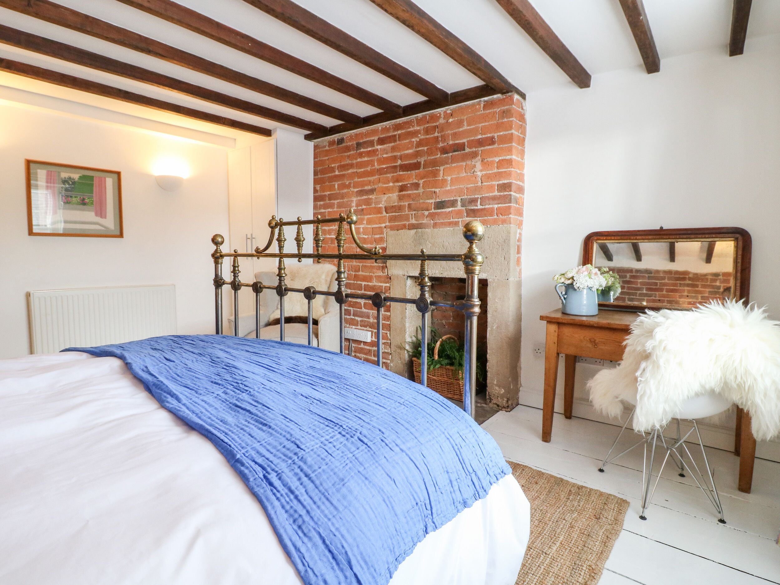 A bedroom with a bed, a brick fireplace, a wooden chair, and a mirror on a dresser.