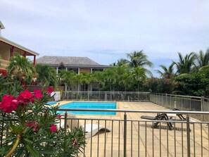 Uma piscina cercada por uma grade de metal, com palmeiras e um edifício ao fundo.