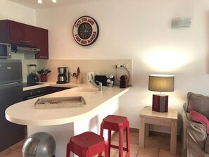 Cozinha compacta com ilha central, micro-ondas, cafeteira e relógio na parede.