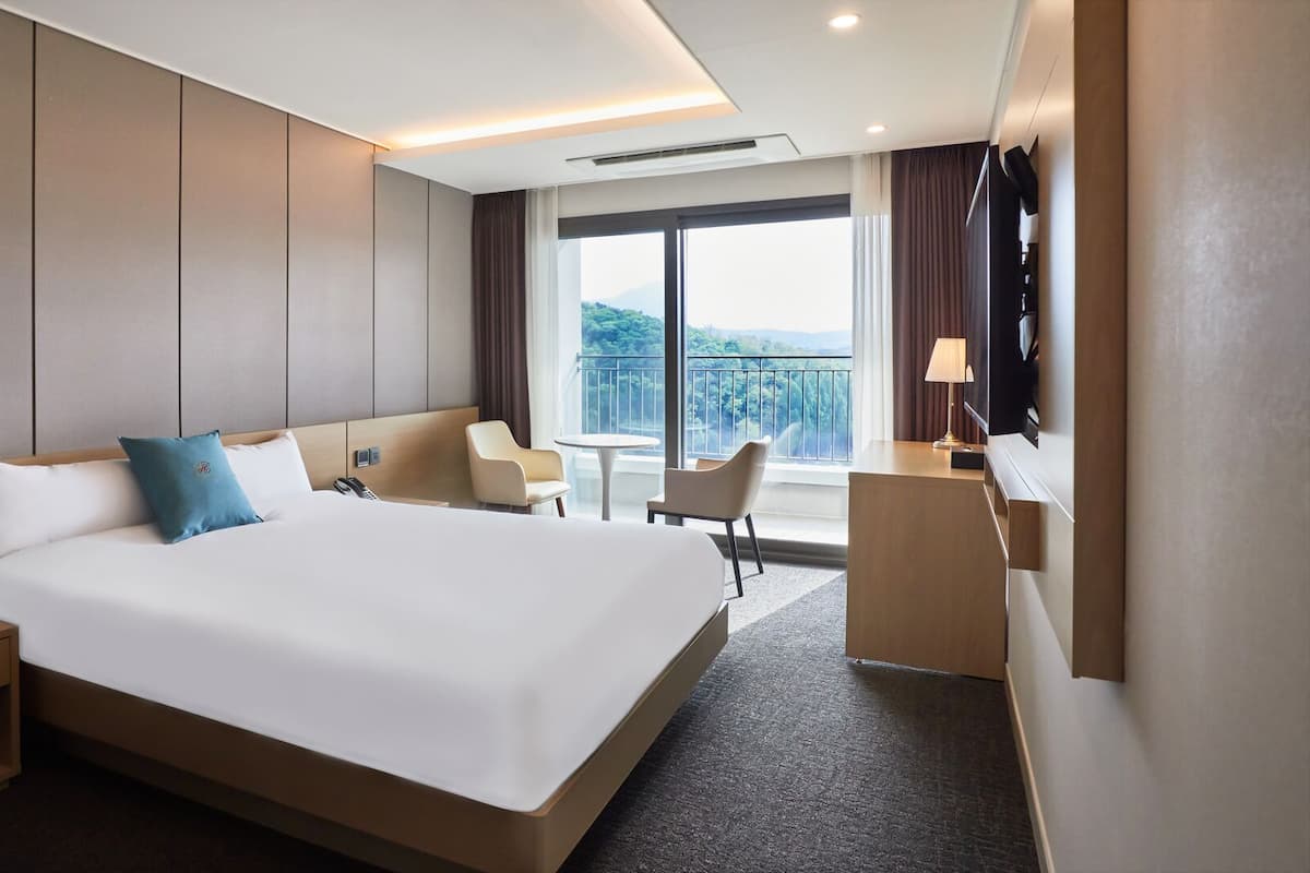 A hotel room with a large bed, bedside tables, a desk, and a view of the outdoors.