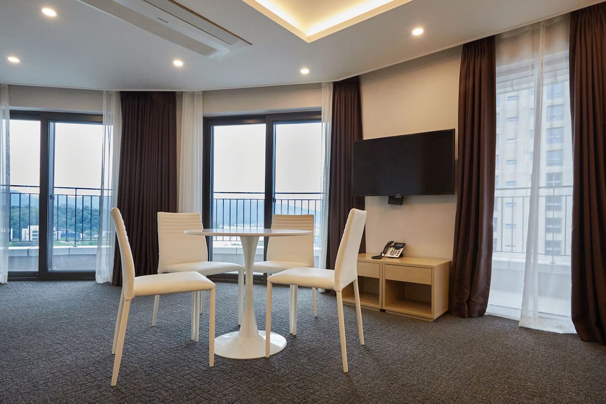 A hotel room with a balcony, a TV mounted on the wall, a desk with a phone, and a bed.