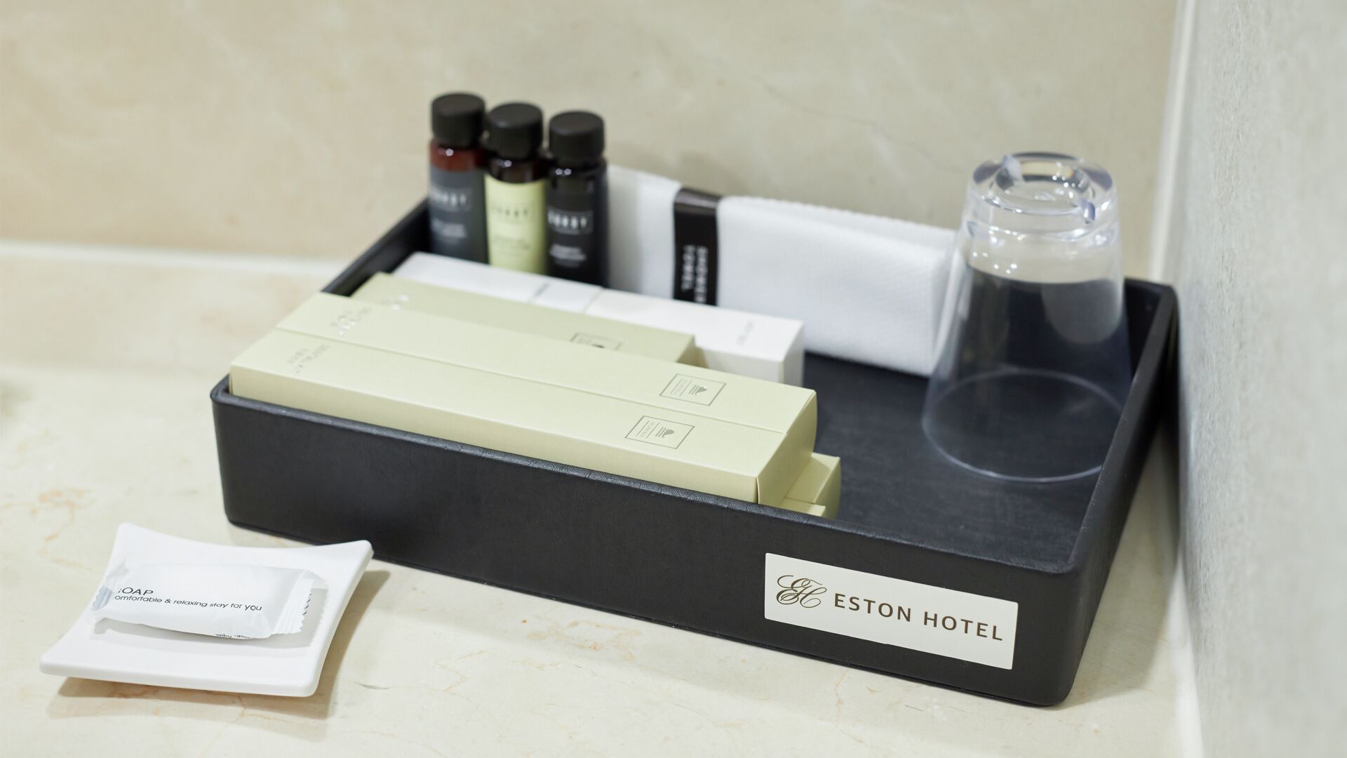 A hotel room's amenities tray with toiletries, a glass, and a white envelope.