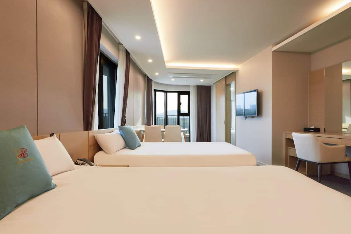 A hotel room with two beds, a desk, a chair, and a TV.
