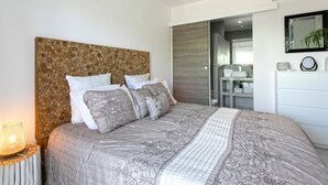 Un dormitorio moderno con una cama grande, cabecera de troncos, mesita de noche con lámpara y cómoda con espejo.