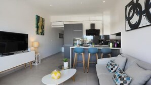 Una sala de estar moderna con televisor de pantalla plana, un sofá, una mesa de centro y una zona de cocina con barra.