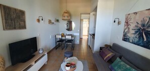 A modern living room with a flat-screen TV, a sofa, a dining area with chairs, a kitchen in the background, and a large mirror on the wall. - Les COQUELICOTS sea view Grimaud (Grimaud)