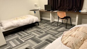 Ein Hotelzimmer mit einem Bett, einem Schreibtisch mit Computer, einem Stuhl und einem kleinen Kühlschrank.