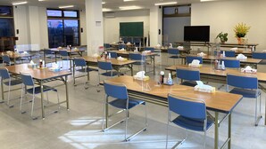 Ein Klassenzimmer mit Reihen von Schreibtischen und Stühlen, einer Tafel, einem Fernseher und einer Topfpflanze.