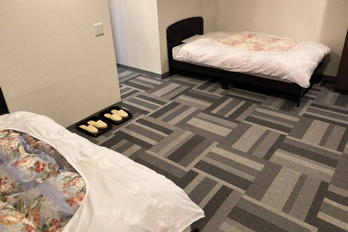 Een hotelkamer met twee bedden, een kamerbreed tapijt met dessin en een dienblad met slippers.