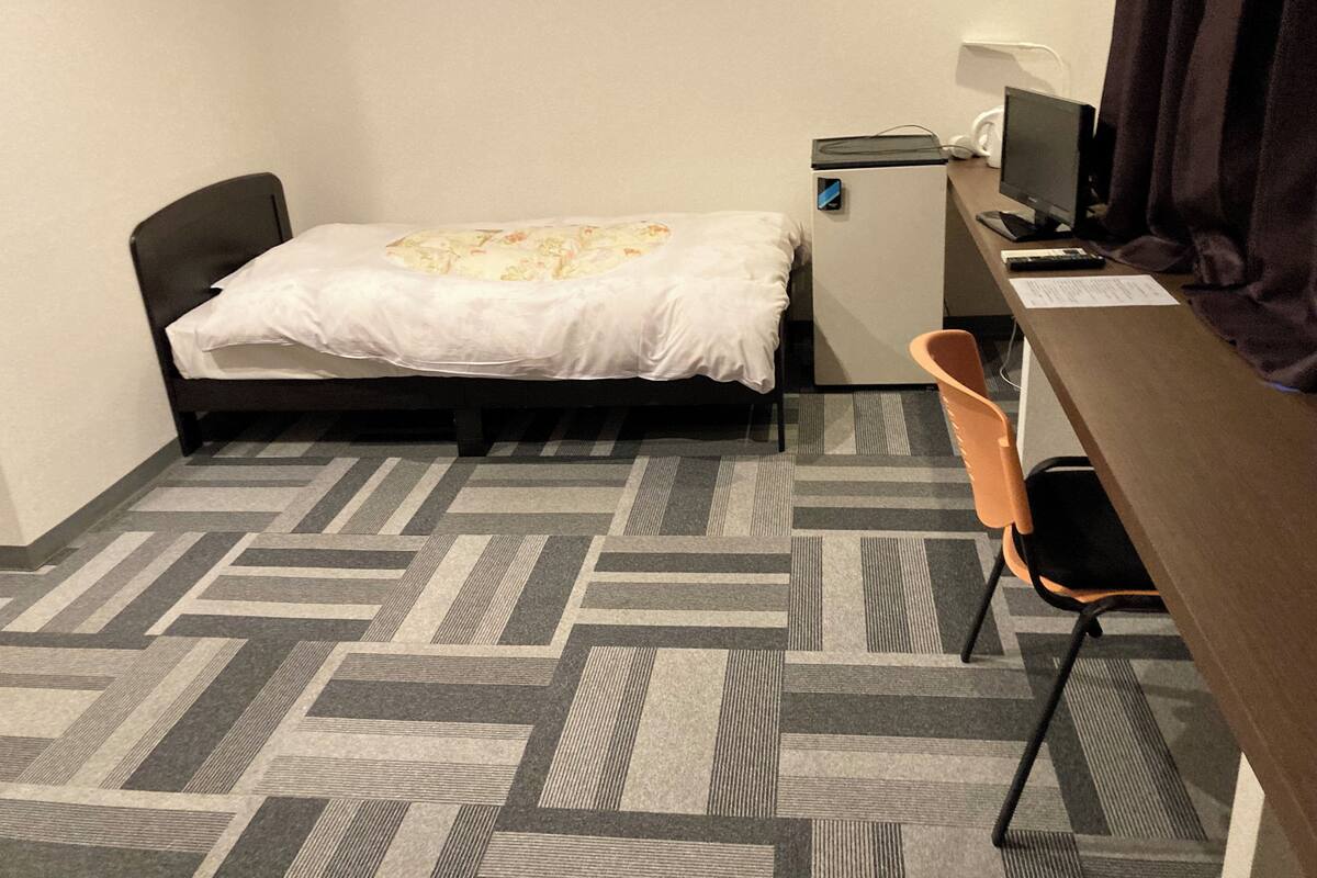 Een kleine hotelkamer met een bed, een bureau, een stoel, een kleine koelkast en een televisie.