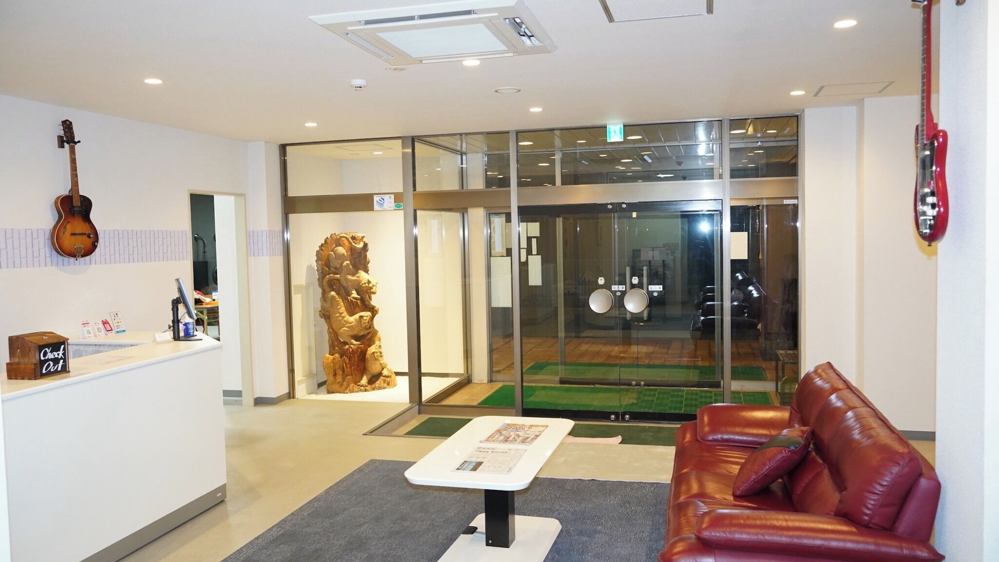 A reception area with a check-out counter, a guitar, a lion statue, a glass door leading to a room, and a leather sofa.